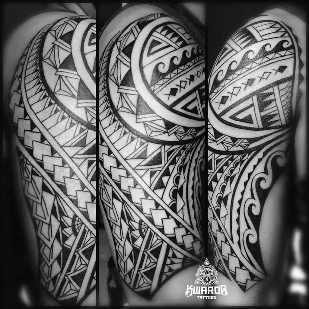 Polynesian upper arm tattoo, showcasing intricate tribal patterns with bold black lines, geometric shapes, and symbolic waves, representing cultural heritage and strength
