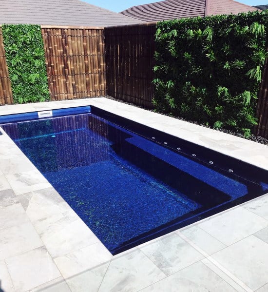 Small rectangular pool with blue tiles, bamboo fencing, and vertical greenery walls featuring vibrant plants.