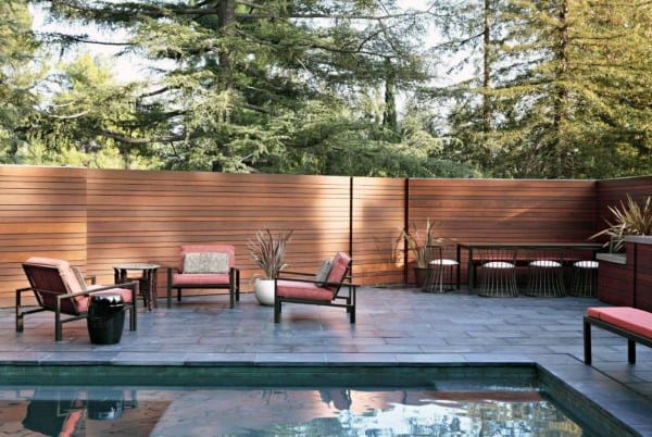 Narrow horizontal wooden fence surrounding a modern backyard with a pool and outdoor seating.