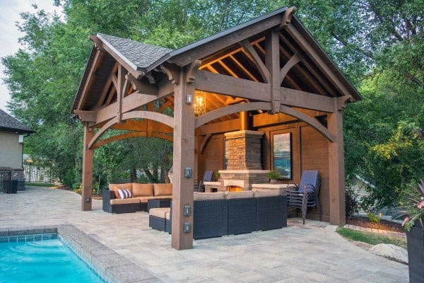 Rustic poolside pavilion with exposed wooden beams, cozy seating, and a stone fireplace for outdoor gatherings.
