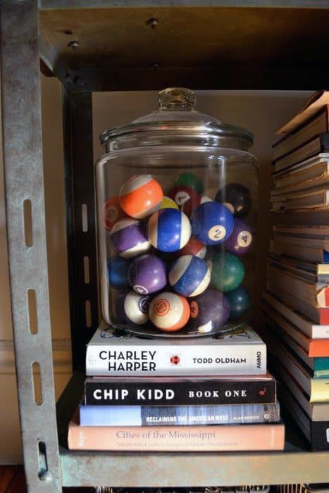 A jar of pool balls on a shelf, resting on a stack of books