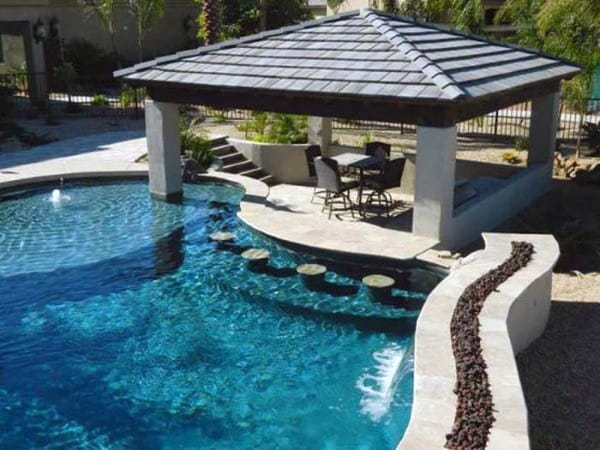 Poolside concrete bar with stools in the water and a covered seating area nearby.