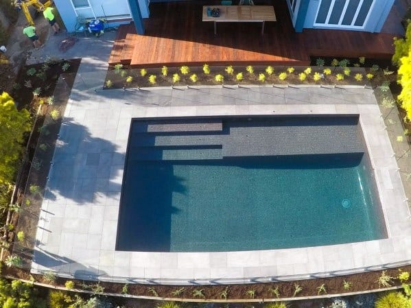 Aerial view of a rectangular backyard pool with surrounding plants and a wooden deck