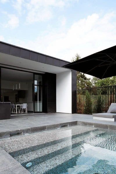 A modern pool design with black and grey mosaic tiles, complemented by minimalist architecture and sleek outdoor furniture.