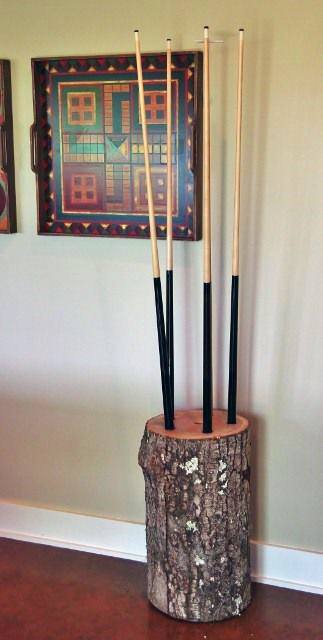 Tree stump cue holder with four pool cues, next to a framed geometric painting on the wall