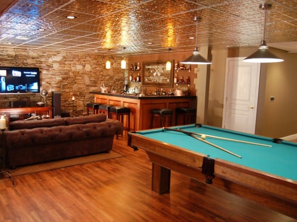Cozy basement with pool table, bar area, stone accent wall, and a couch facing a wall-mounted TV