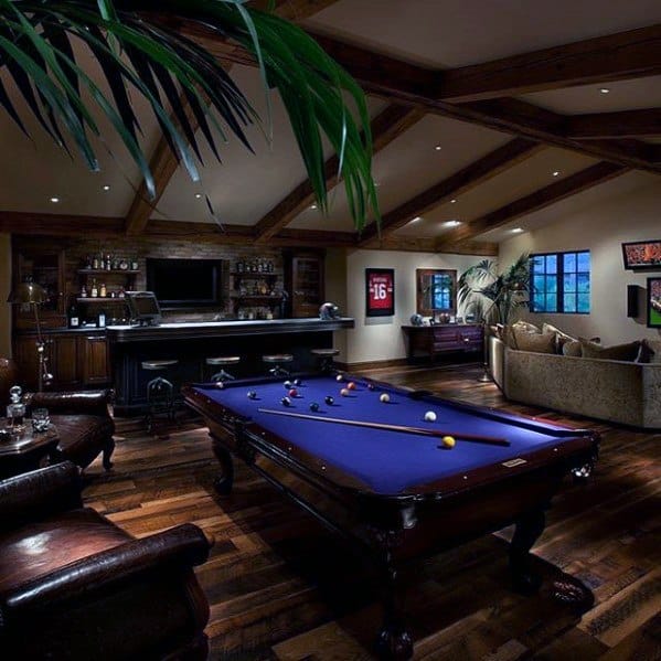 A cozy man cave with a pool table, bar, seating area, dim lighting, warm ambiance, and wooden ceiling beams