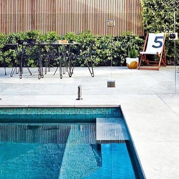 Modern pool with turquoise mosaic tiles, glass fencing, and a stylish outdoor seating area.