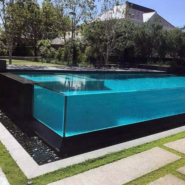 Infinity-edge pool with clear glass walls, turquoise tiles, and a modern landscaped garden.