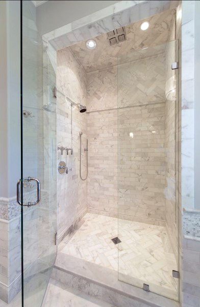 Herringbone marble tile shower with glass enclosure and rainfall showerhead.