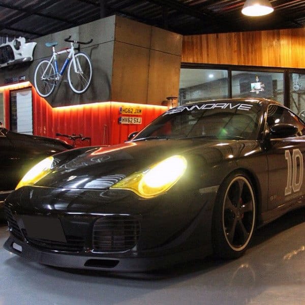 Sleek garage featuring a Porsche, warm wood paneling, mounted bike decor, and glowing accent lighting.