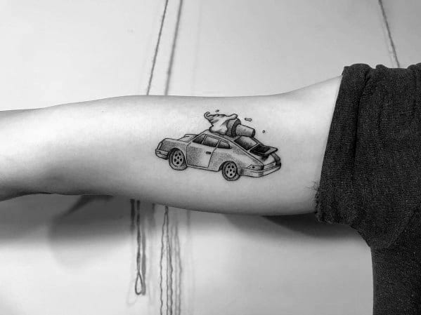 Playful, minimalist Porsche tattoo on the inner arm, featuring luggage and whimsical details for a fun road-trip vibe.