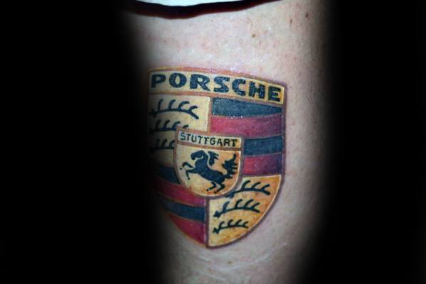 Colorful Porsche crest tattoo with rich black, red, and gold details, partially shadowed for contrast.