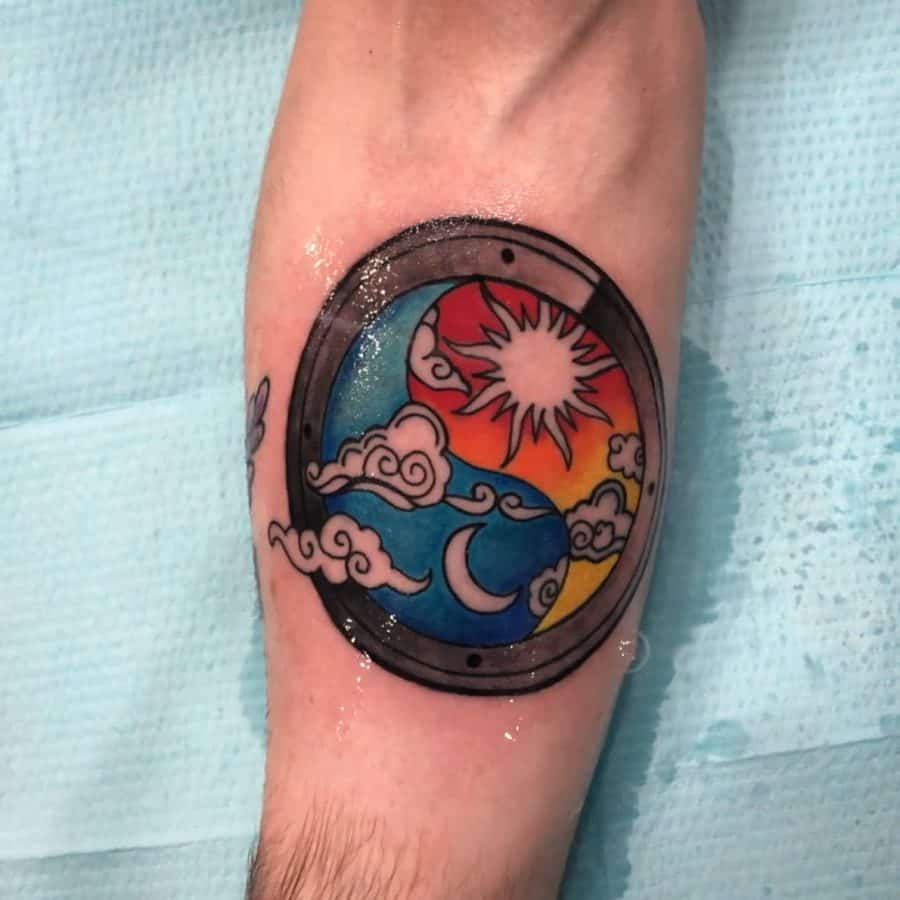 Tattoo of a sun and moon inside a porthole, featuring vibrant colors, swirling clouds, and a mix of day and night elements.