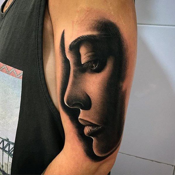 Realistic face tattoo on a person's upper arm, exhibiting detailed shading and depth
