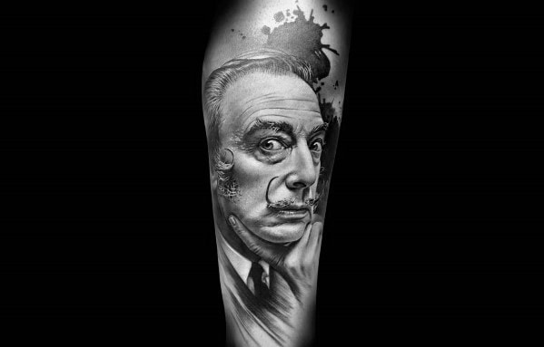 Hyper-realistic tattoo of Salvador Dalí showcasing his signature mustache and surreal expression, complemented by artistic ink splatter details in the background