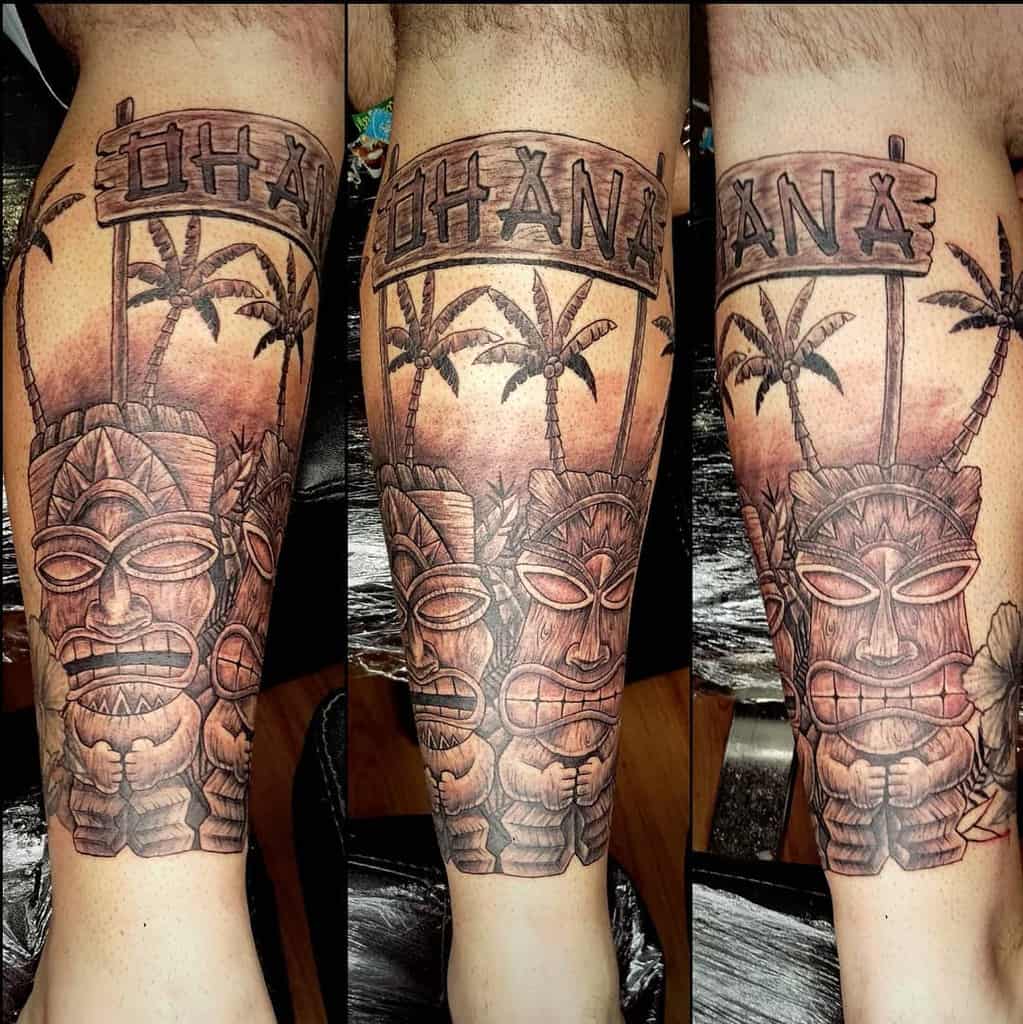 Detailed Polynesian-style tattoo featuring a tiki mask, palm trees, and an 'Ohana' sign, symbolizing family and Hawaiian culture.
