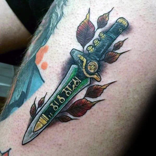 Bold Dragon Dagger tattoo with gold and green details, surrounded by falling red leaves and dynamic shading on the upper arm.