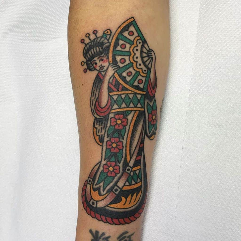 Traditional-style Geisha tattoo on the forearm, featuring a bold color palette, floral kimono, and a decorative fan with classic black outlines.