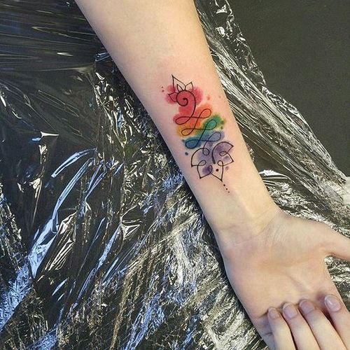Unalome tattoo with a lotus and vibrant rainbow watercolor on the forearm, symbolizing spiritual growth, balance, and self-expression.