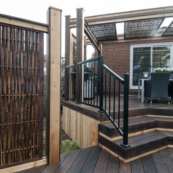 Dark bamboo privacy fence with wooden frame next to a modern raised deck with metal railing.