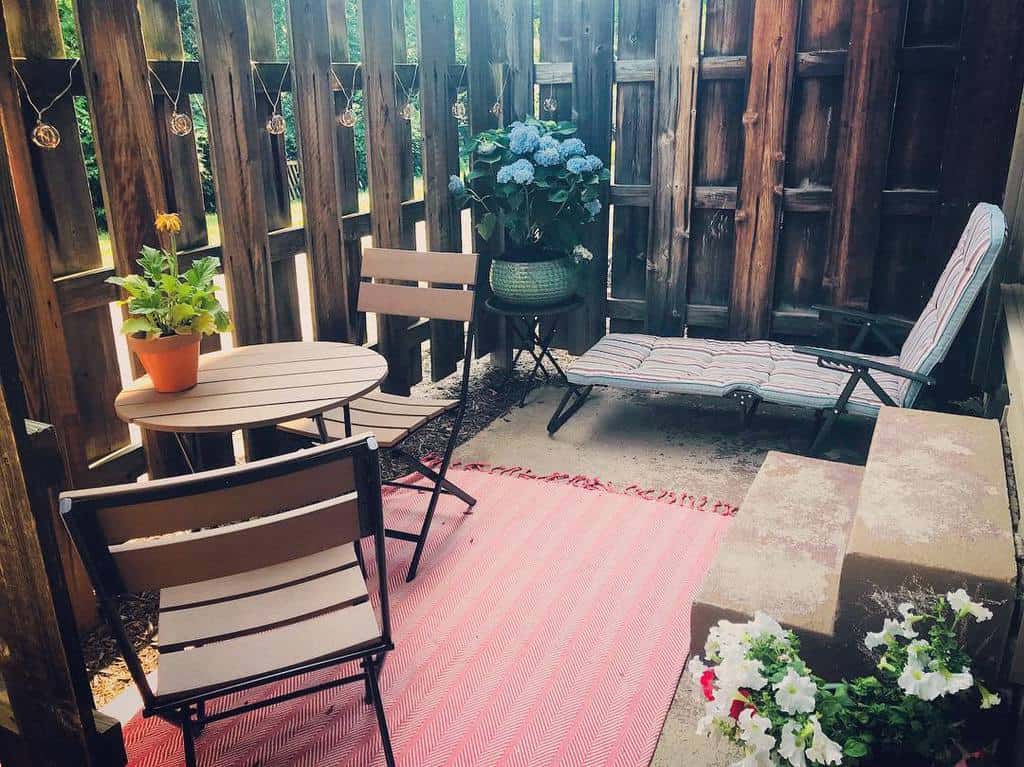 Small patio with wooden fencing, a cozy seating area, potted plants, and a red outdoor rug.