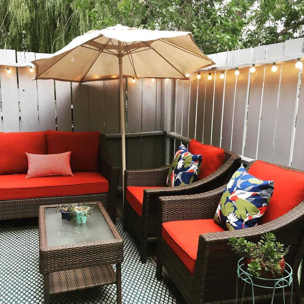 Cozy patio with wicker chairs, red cushions, colorful pillows, and a beige umbrella.