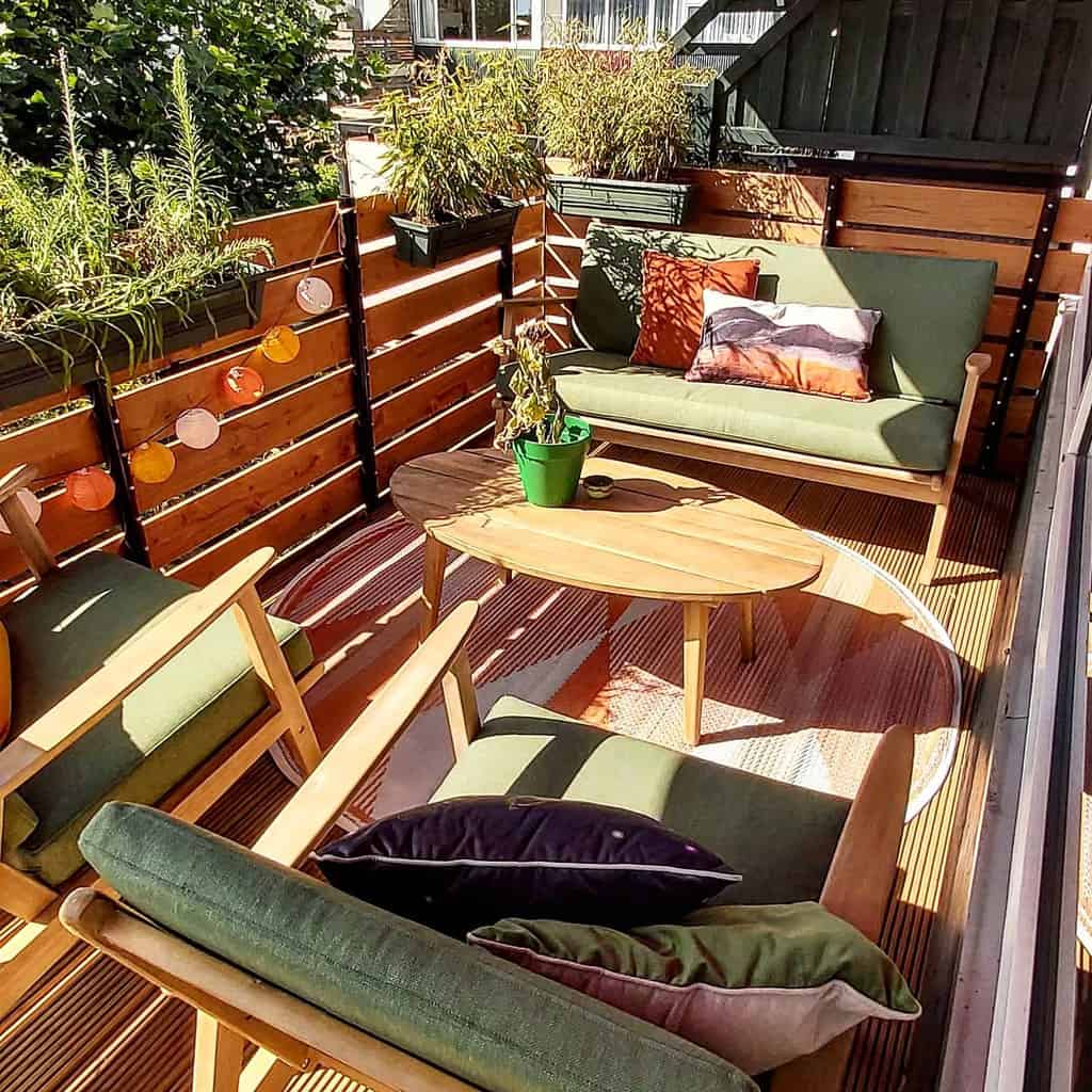 Wooden patio with green cushioned furniture, plants, and a small round table.