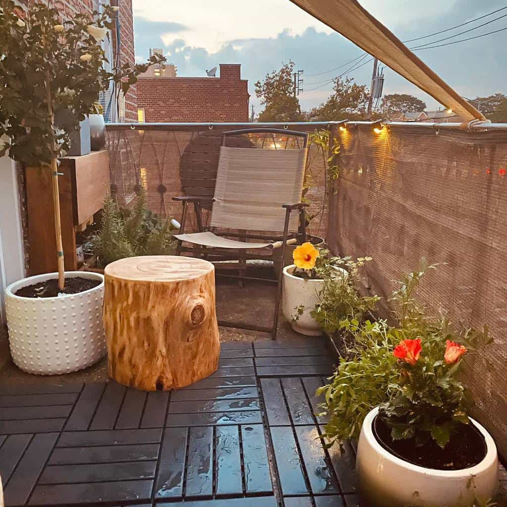 Cozy balcony with wood stump table, folding chair, potted plants, and string lights.