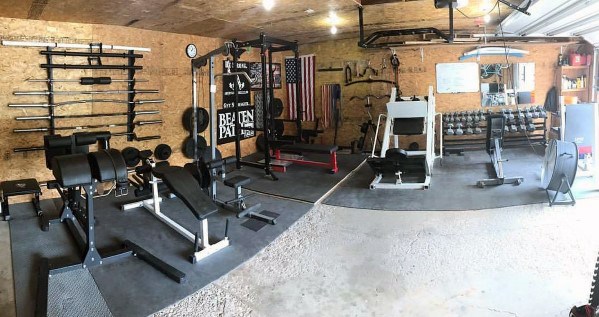 Spacious garage gym with power rack, barbell storage, benches, dumbbells, and American flag decor.