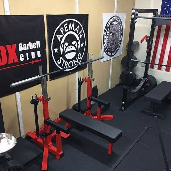 Compact home gym with red bench press setup, weight rack, and motivational wall banners.