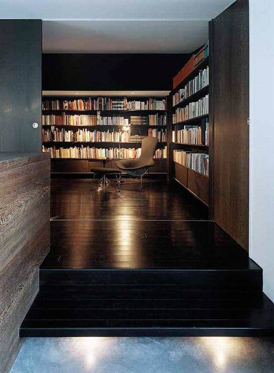 Cozy library with dark wooden shelves, a variety of books, and a lounge chair on the polished library floor