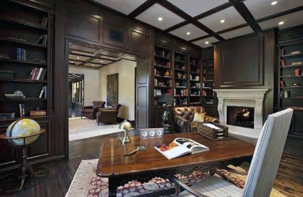 Luxurious home library with dark wood paneling, bookshelves, a fireplace, leather sofa, and a large wooden desk