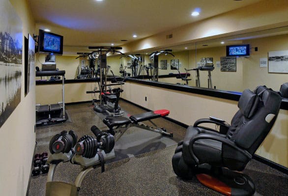 Home gym with exercise equipment, dumbbells, treadmill, bench, and massage chair set against mirrored home walls