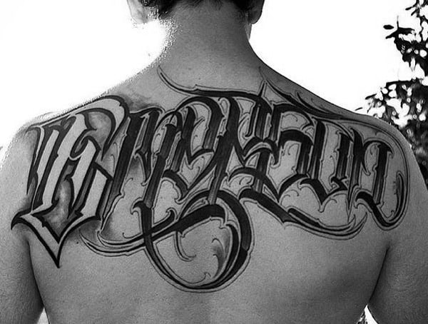 Man's back with intricate black tattoo of stylized letters across shoulders