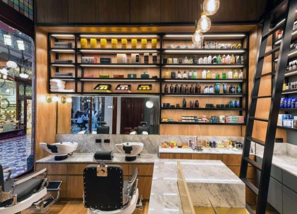 Barbershop with marble counters, black chairs, and wall shelves displaying grooming products.