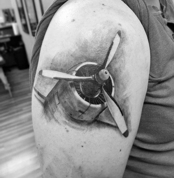 Realistic black and grey upper arm tattoo of an aircraft propeller engine, featuring detailed shading and depth for a mechanical and dynamic look.