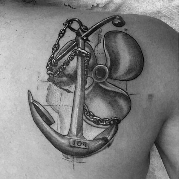 Black and grey chest tattoo of an anchor and propeller entwined with a chain, featuring detailed shading and sketch-style background elements.