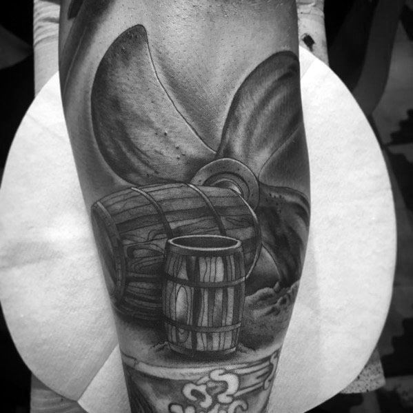 Black and grey tattoo featuring a large ship propeller with wooden barrels, detailed shading, and a nautical theme for a bold maritime design.