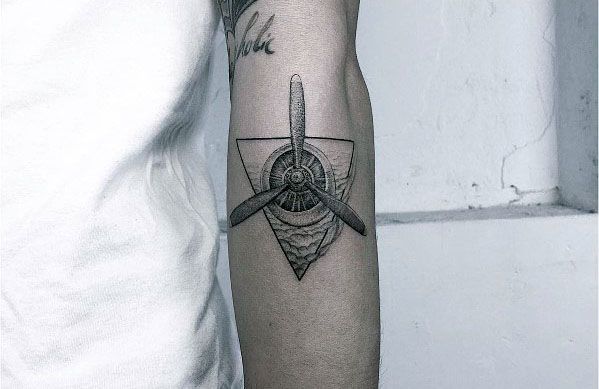Black and grey forearm tattoo of a detailed aircraft propeller within a geometric triangle, featuring fine linework and shading for a modern aviation look.