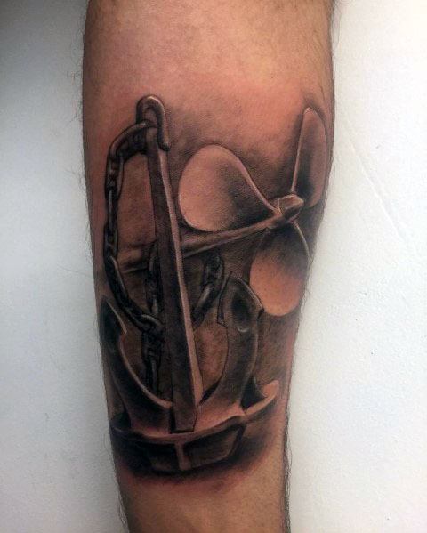 Realistic black and grey forearm tattoo of an anchor wrapped in a chain with a ship propeller in the background, featuring deep shading and fine details.