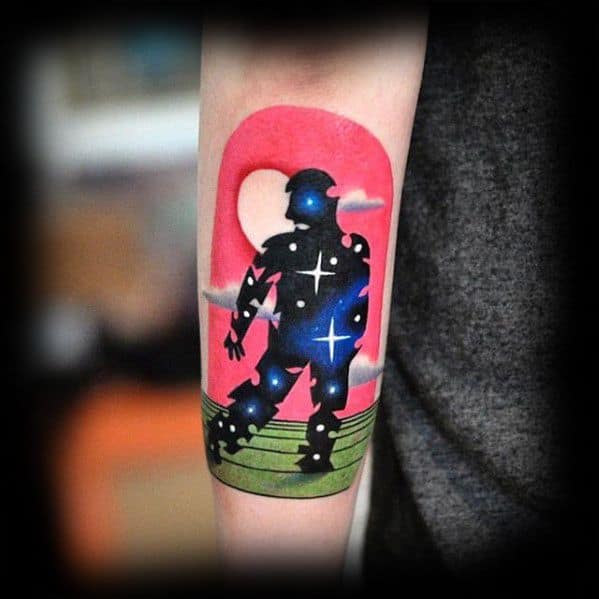 Colorful tattoo of a silhouetted astronaut figure filled with stars and galaxies, set against a pink and red sky with clouds and a green landscape.