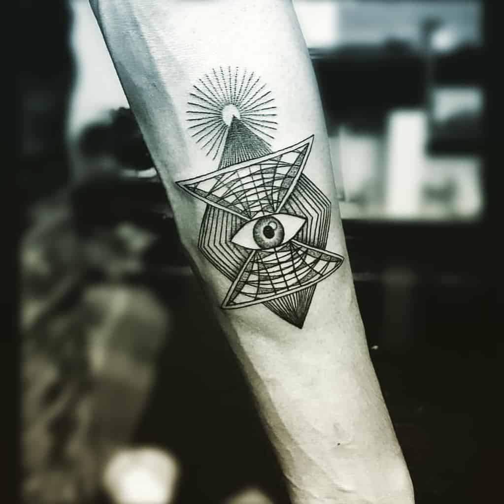 Tattoo of an all-seeing eye within geometric patterns, with radiating lines above, inked in fine black lines on the forearm.