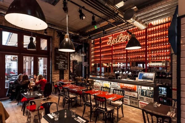 Cozy restaurant with brick walls, industrial lighting, vintage decor, and a vibrant bar with red-lit bottle shelves