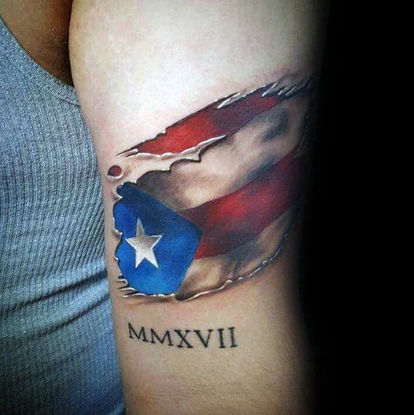 Puerto Rican flag tattoo with a ripped skin effect and Roman numerals "MMXVII," symbolizing pride, heritage, and a significant year.
