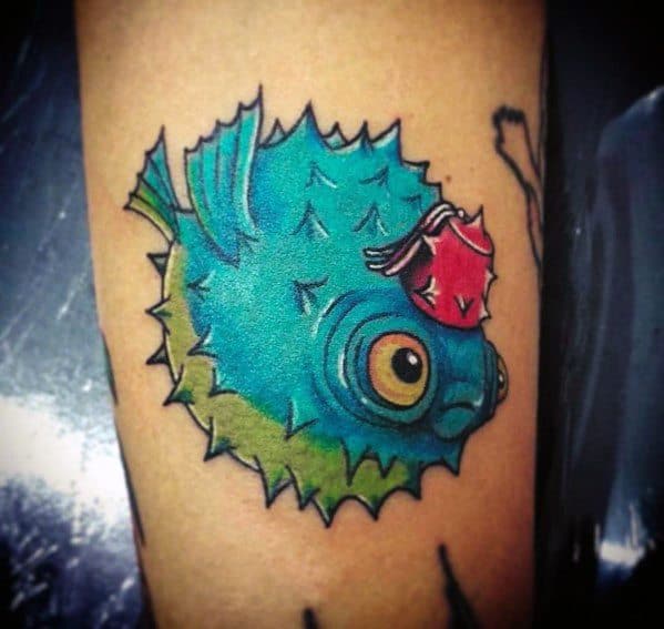 Bright blue pufferfish tattoo with bold black outlines, green shading, and a red seashell detail, creating a vibrant and playful design.