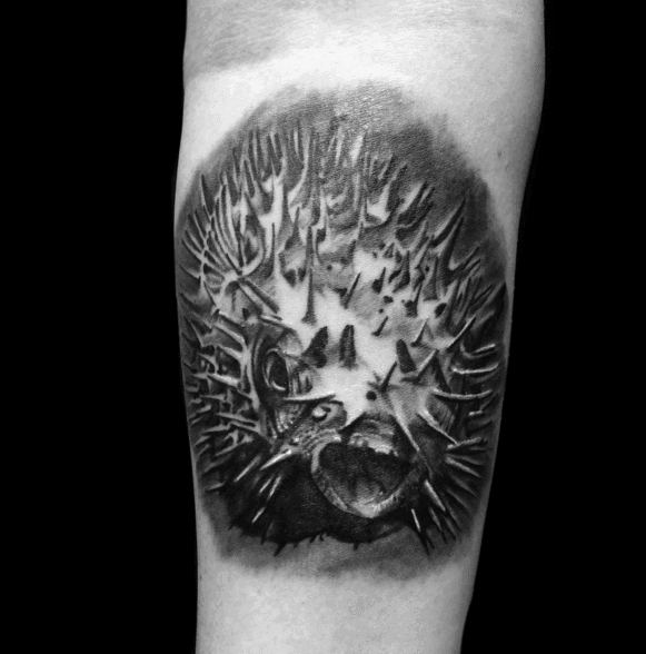 Black and grey pufferfish tattoo with intense shading, sharp spikes, and a dramatic expression, creating a bold and highly detailed design.