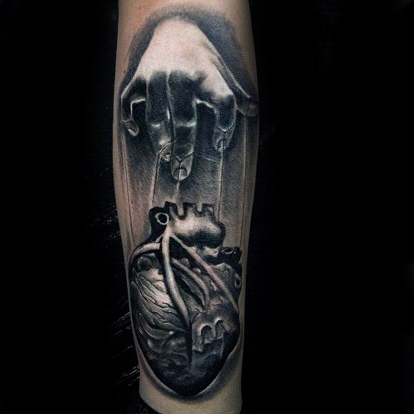 Realistic black and grey tattoo of a hand controlling an anatomical heart with strings, symbolizing emotional manipulation or control.