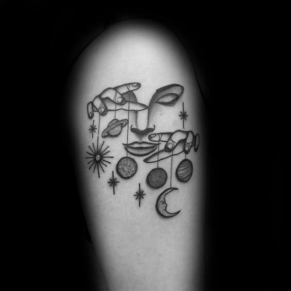 Minimalist celestial puppet tattoo of a face with hands controlling planets, stars, sun, and moon, symbolizing cosmic balance and influence.