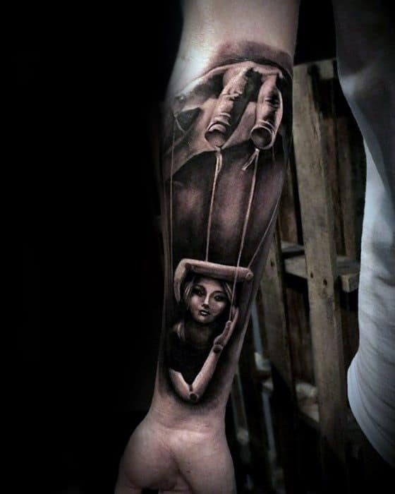 Realistic black and grey puppet tattoo of a large hand controlling a female marionette, symbolizing manipulation, control, or power dynamics.